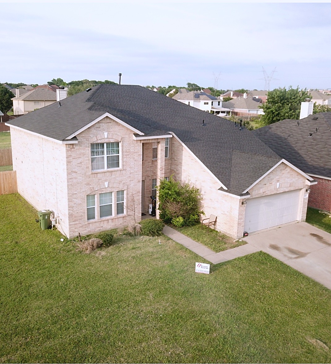 Two-story tan brick home with a finished dark shingle roof
